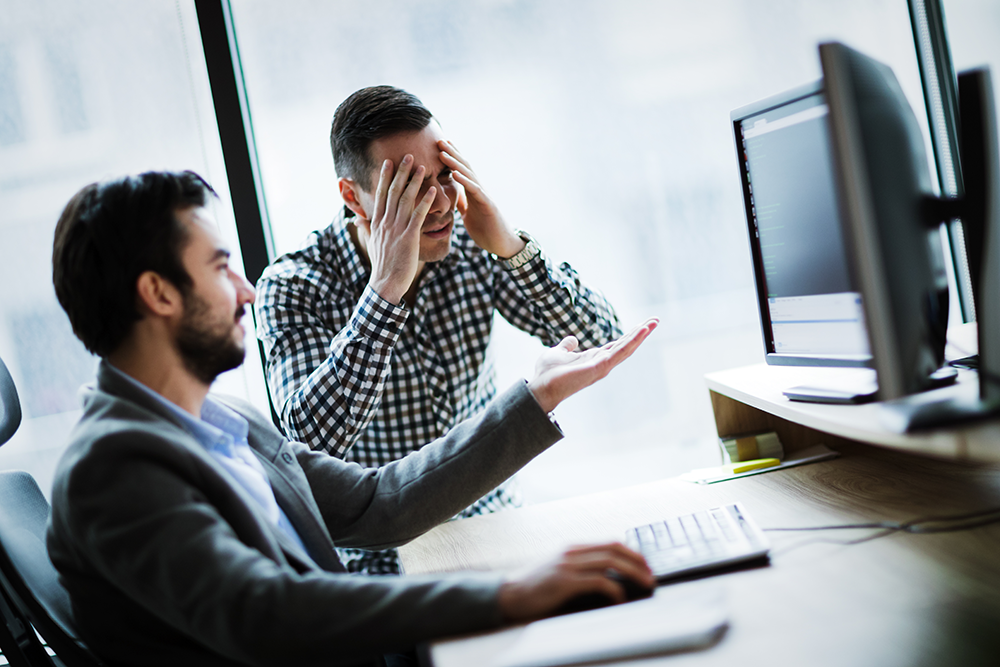 Two frustrated coworkers in an office look at a computer monitor with anger.