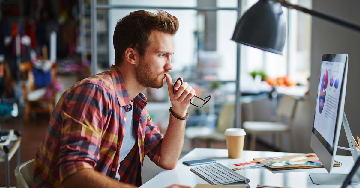 Male designer carefully reviews colorful charts on his computer screen.