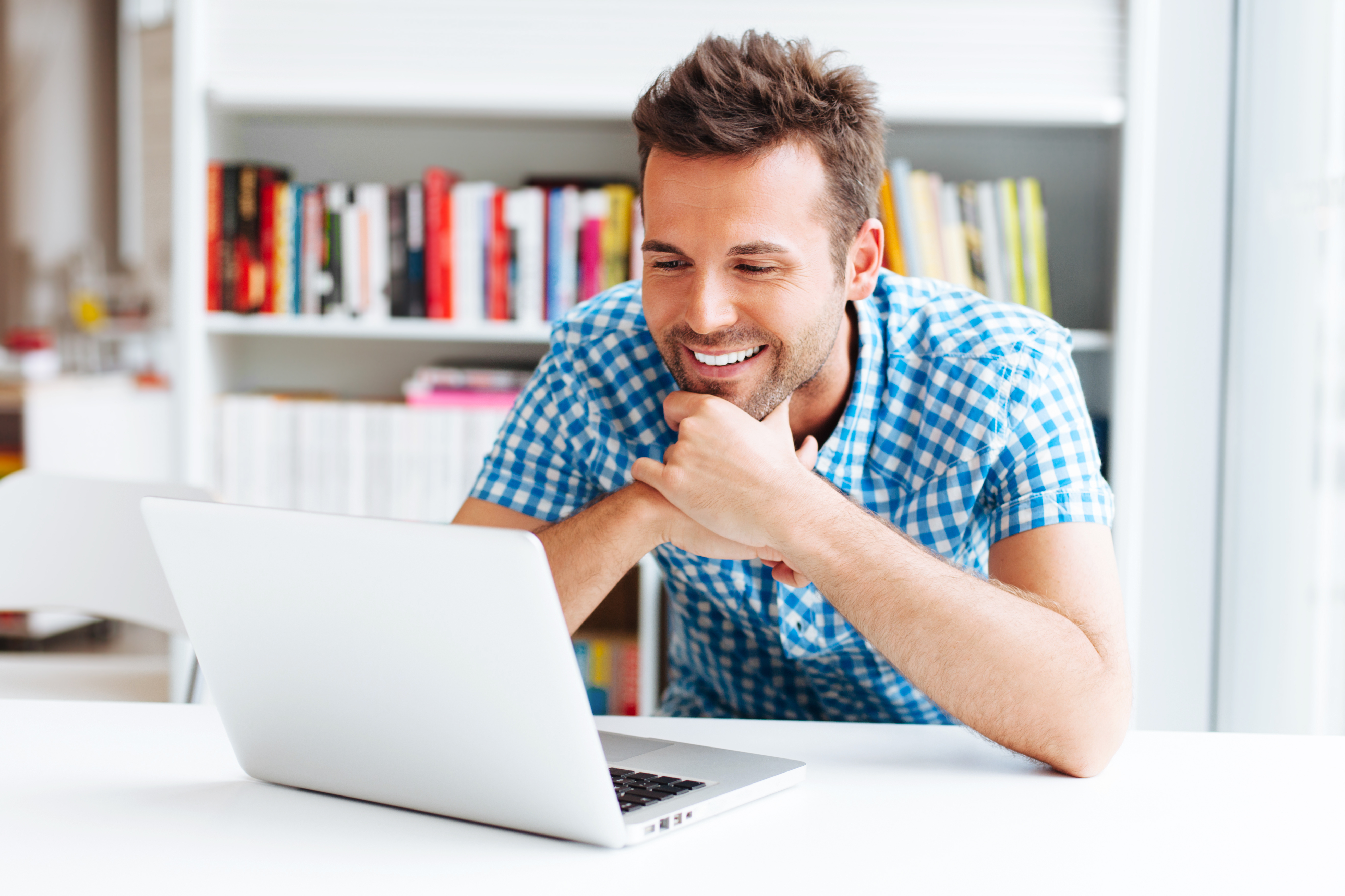 man in white office smiling as he looks at his laptop